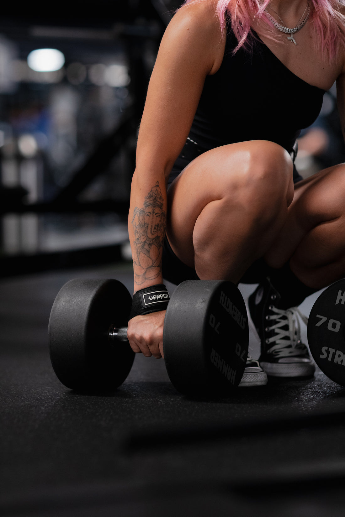 woman holding dumbbell wearing uppper lifting straps